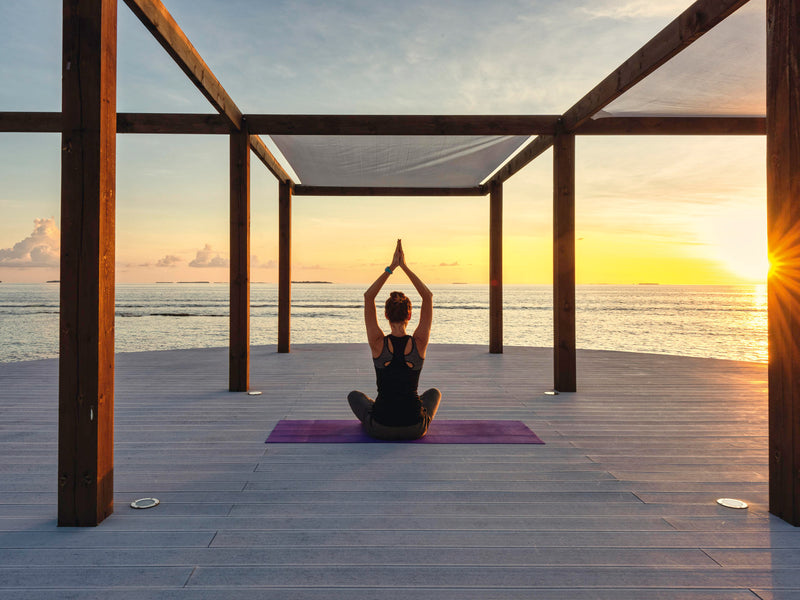Yoga on a deck at sunset at Kuredhivaru Resort & Spa Maldives.