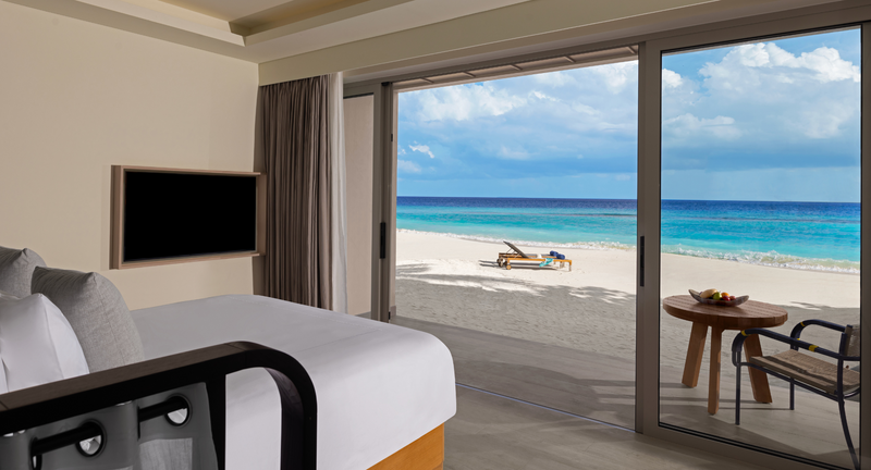 A Premium Beachfront Room bedroom at Avani+ Fares Maldives, with sliding doors opening straight onto the sand.