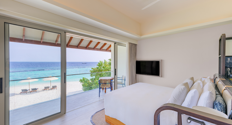 A Premium Ocean View Room bedroom at Avani+ Fares Maldives, looking through sliding doors to the beach and sea.