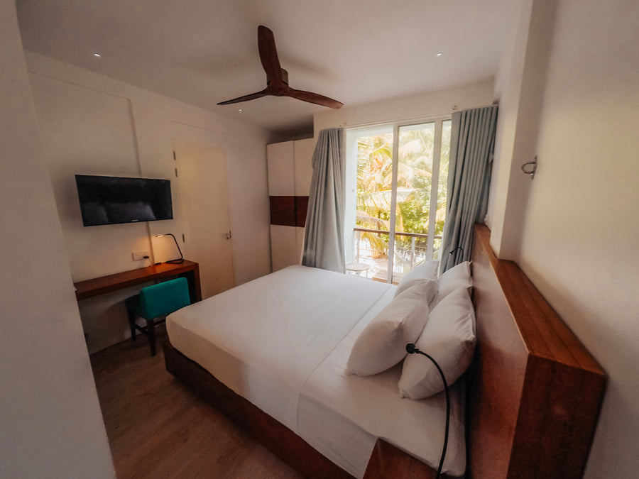 Compact Room at Bliss Dhigurah with a queen bed, desk, ceiling fan and balcony door