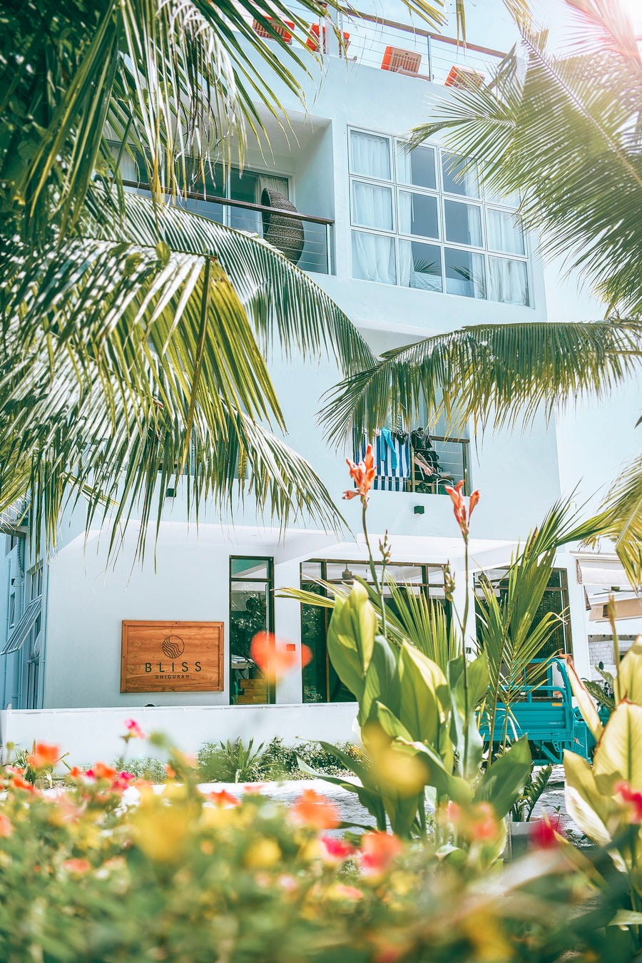 Entrance to Bliss Dhigurah with the hotel sign, palms and flowering plants