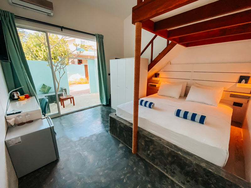 Loft by Bliss on Dhigurah, a king bed below a wooden stair to the upper beds, opening onto a garden