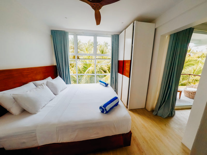 Suite at Bliss Dhigurah with a king bed and full-height windows onto palms