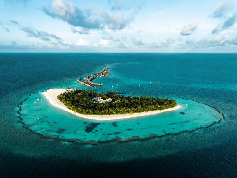 Constance Halaveli, North Ari Atoll: the island from the air, white beach and dense palms set in a pale lagoon