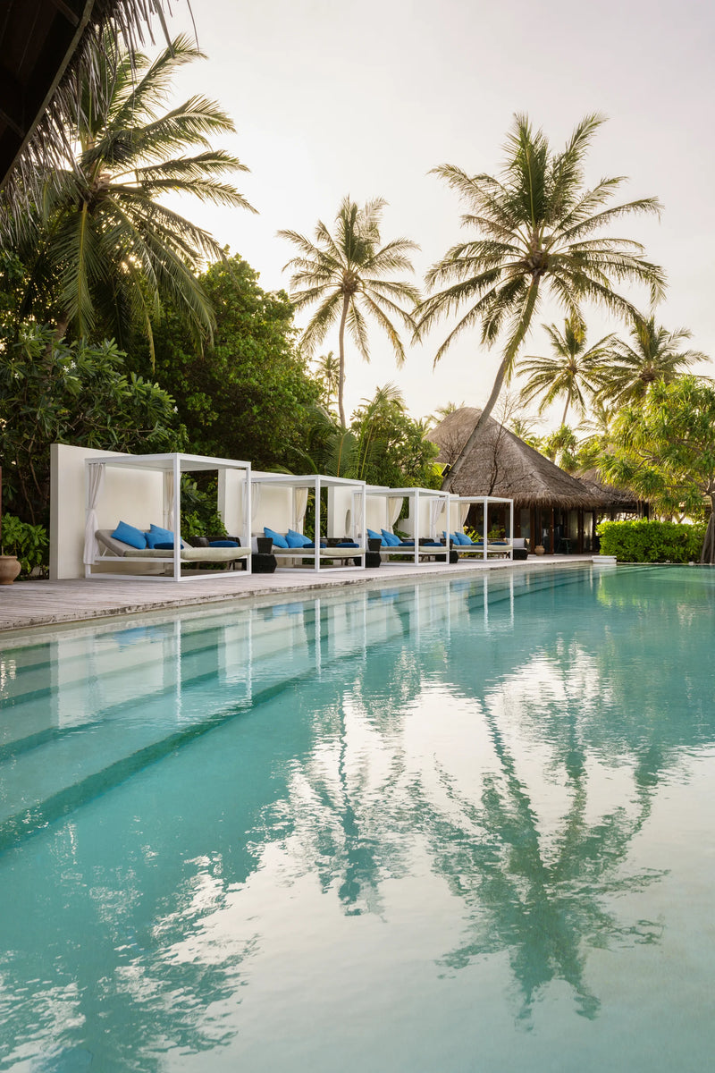 Constance Halaveli, North Ari Atoll: white cabanas with blue cushions along the edge of the main pool