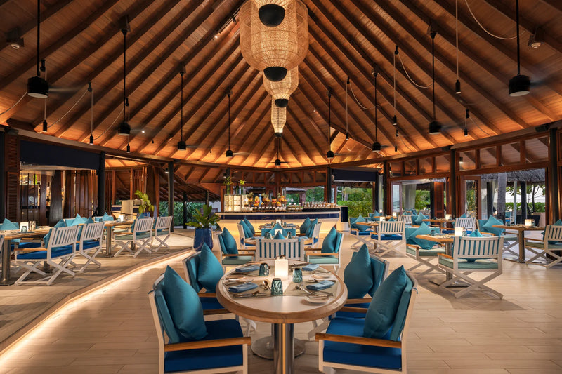 Constance Halaveli, North Ari Atoll: Jahaz restaurant dining room under a high timber ceiling, blue chairs around set tables