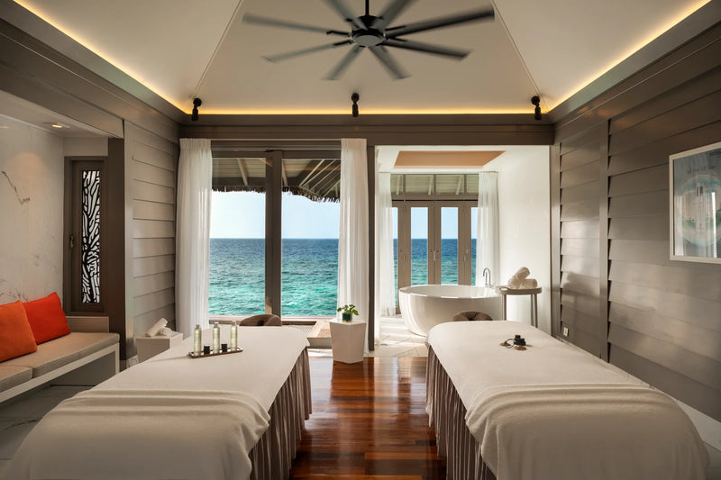 Constance Halaveli, North Ari Atoll: a couple's spa treatment room with two beds and floor-to-ceiling windows onto the sea