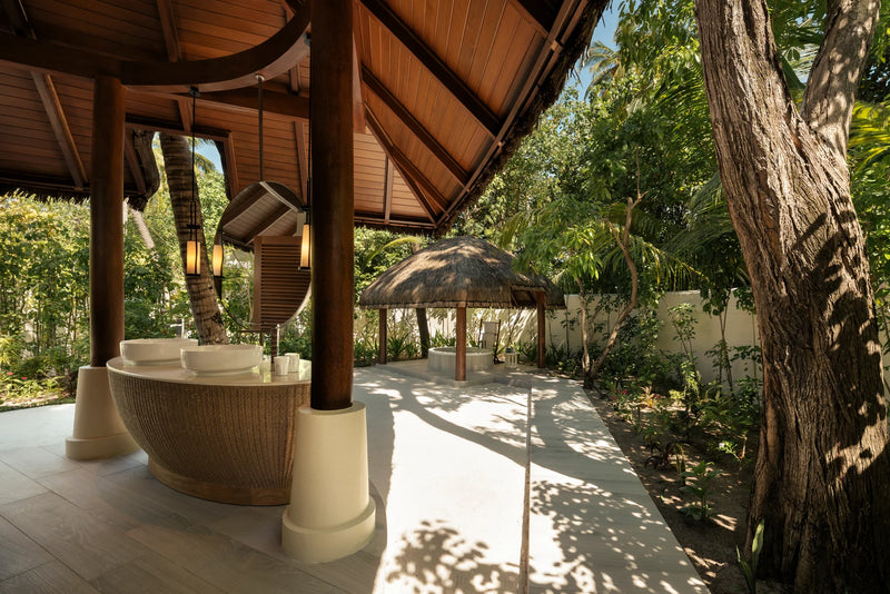 Constance Halaveli, North Ari Atoll: shaded outdoor seating under a thatched roof in a Beach Villa garden