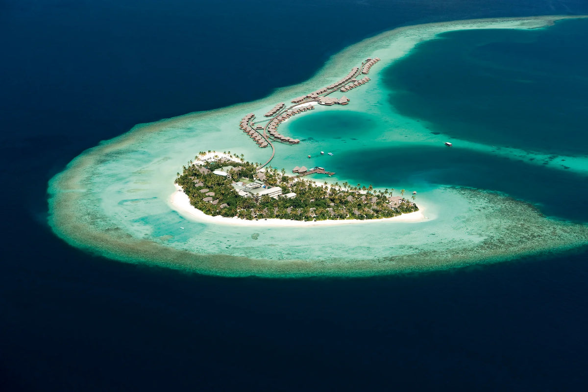 Constance Halaveli, North Ari Atoll: aerial view of the island inside its reef, water villa jetties reaching out across the lagoon