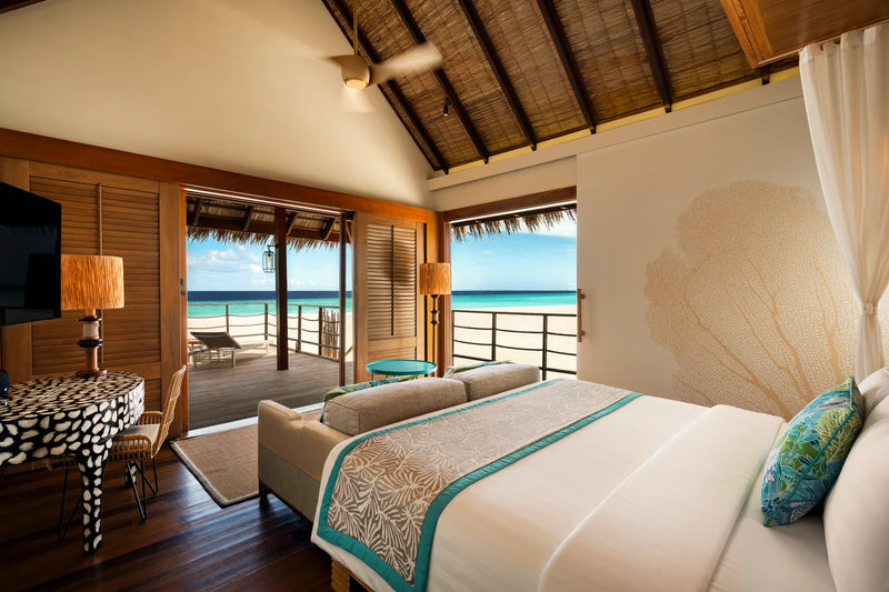 Constance Moofushi, South Ari Atoll: Senior Sand Villa bedroom with a sofa and wide doors open to the deck and the sea