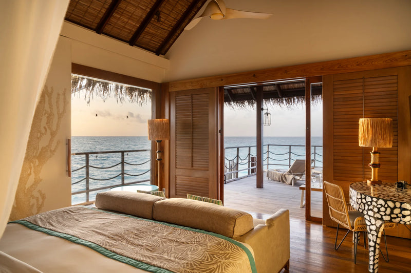 Constance Moofushi, South Ari Atoll: Senior Water Villa bedroom with a sofa at the foot of the bed and doors open to the deck