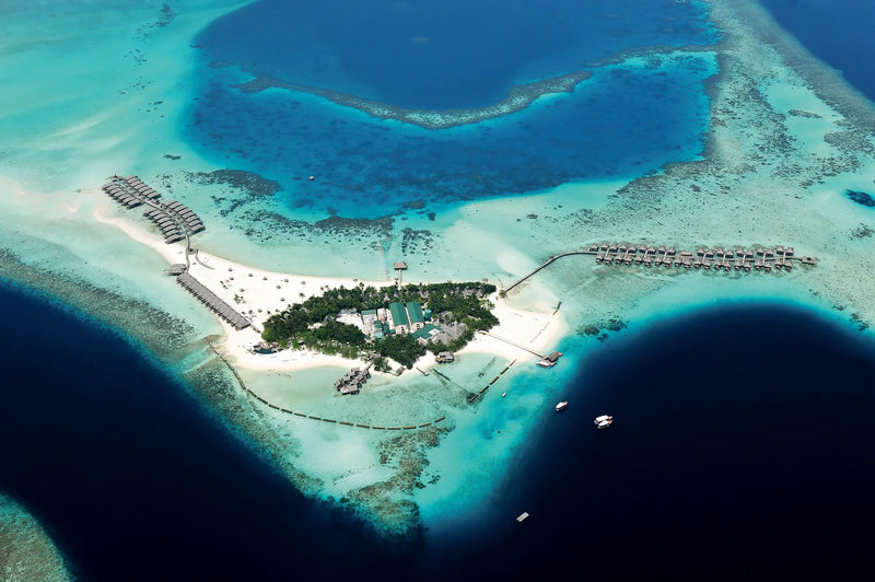 Constance Moofushi, South Ari Atoll: aerial view of the small island ringed by its lagoon and reef, water villa jetties off both ends