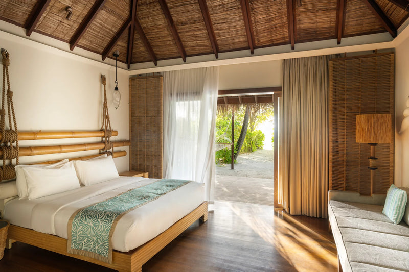 Constance Moofushi, South Ari Atoll: Beach Villa bedroom under a thatched roof, doors open to the garden and the sand
