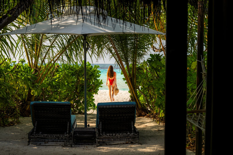 Constance Moofushi, South Ari Atoll: two loungers under an umbrella in a Beach Villa garden, with a sandy path through the greenery to the sea