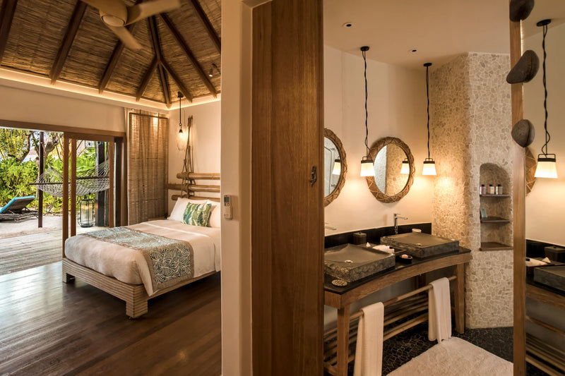 Constance Moofushi, South Ari Atoll: Beach Villa bedroom seen through to the bathroom, round mirrors over twin basins