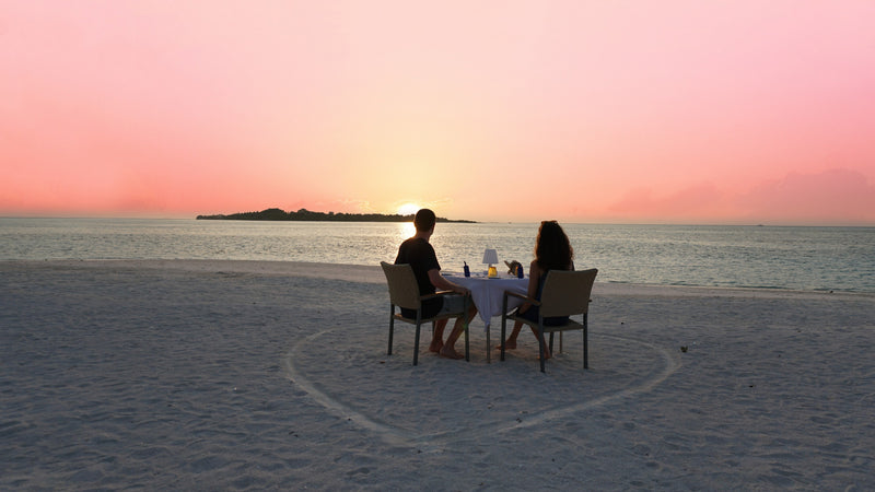 A couple dining on the sand at sunset at Cocoon Maldives.