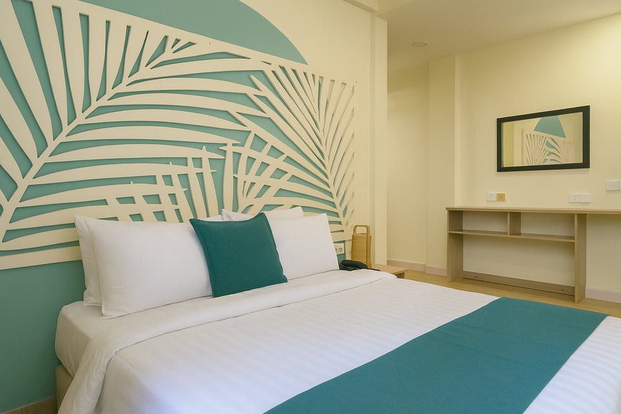 Deluxe room at KUE Hotel with a queen bed under a palm-leaf headboard mural