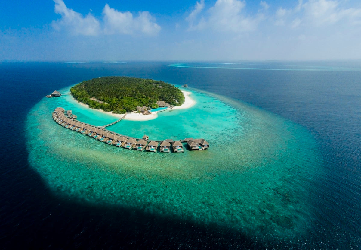Dusit Thani Maldives from the air, the island and its overwater villa crescent.