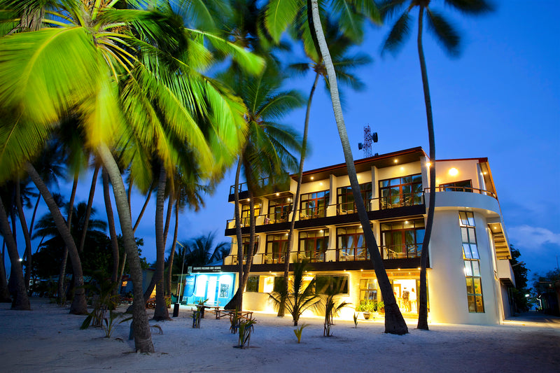 Kaani Beach Hotel lit up at dusk behind the palms