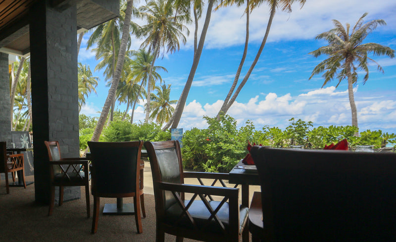 Outdoor dining terrace under palm trees at Kaani Grand Seaview