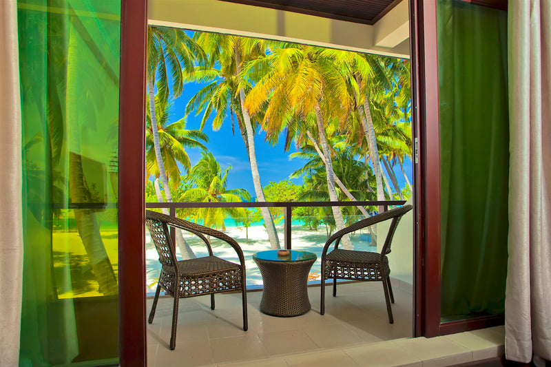 Balcony with two chairs looking through palm trees to the sea at Kaani Beach Hotel