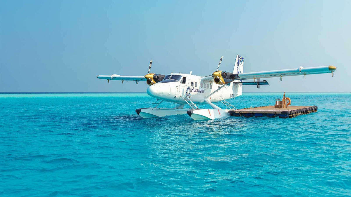A seaplane in Hurawalhi Maldives livery moored at a floating pontoon on turquoise water.