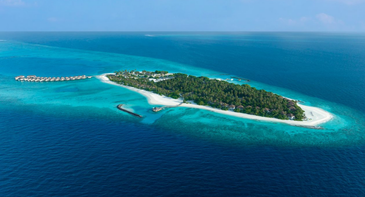 The whole island from the air at Avani+ Fares Maldives, palm-covered and ringed by white sand, with a jetty of overwater villas.