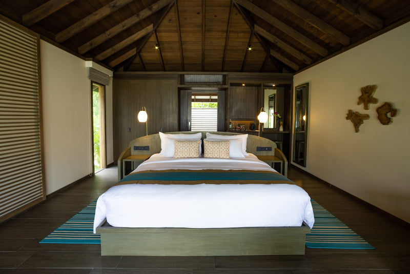 Jawakara Islands Maldives, Lhaviyani Atoll: a Mabin beach villa bedroom with a king bed under a timber ceiling