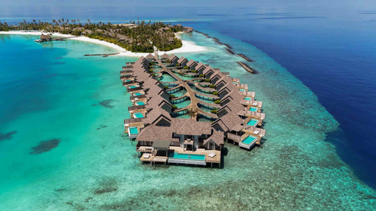 The overwater villas at ananea Madivaru Maldives from the air, two rows of thatched roofs over the lagoon