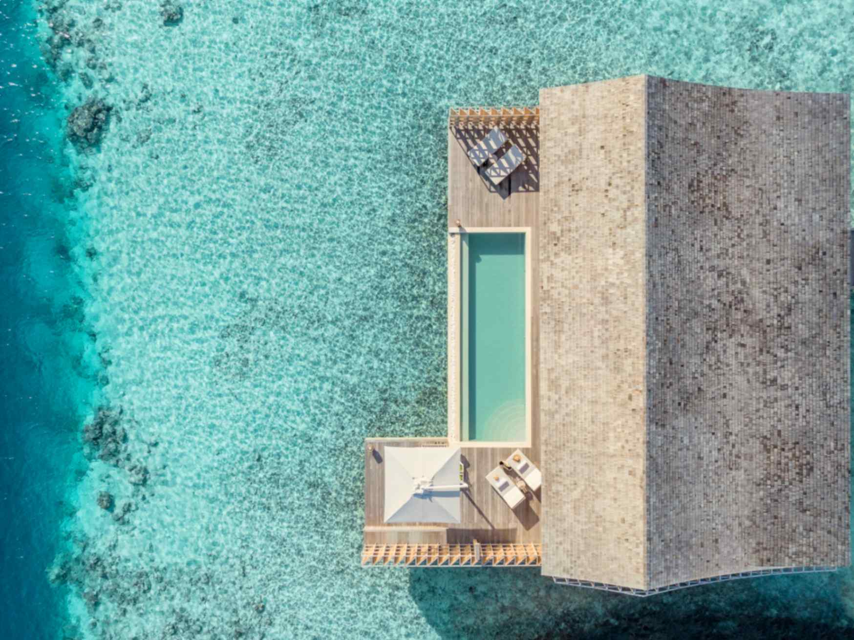 Kudadoo Maldives Private Island, Lhaviyani Atoll — aerial view looking straight down on an overwater residence, its private pool and sun deck set against the turquoise reef edge