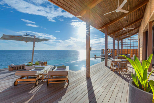 Kudadoo Maldives Private Island, Lhaviyani Atoll — timber deck with sun loungers under a white cantilevered parasol, beside an infinity pool that runs to the ocean edge