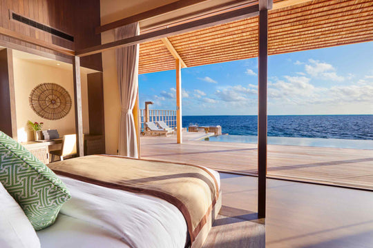 Kudadoo Maldives Private Island, Lhaviyani Atoll — bed facing floor-to-ceiling glass that opens onto the residence deck and infinity pool above deep blue water