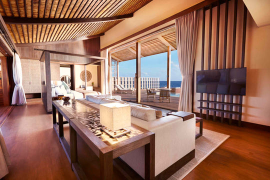 Kudadoo Maldives Private Island, Lhaviyani Atoll — residence living area with sofa, long console table and wall-mounted television, opening onto the deck and ocean