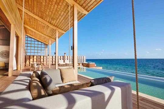 Kudadoo Maldives Private Island, Lhaviyani Atoll — rope-hung swing sofa on the deck beneath a bamboo-lined ceiling, alongside the residence&