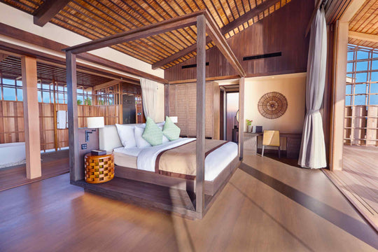 Kudadoo Maldives Private Island, Lhaviyani Atoll — four-poster bed in a timber-lined bedroom, with a writing desk and the bathtub visible through the doorway