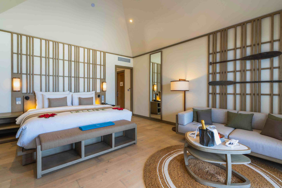 Kagi Maldives Resort &amp; Spa, North Malé Atoll — villa interior showing the king bed alongside the seating area, with a sofa, round rug and champagne on the coffee table