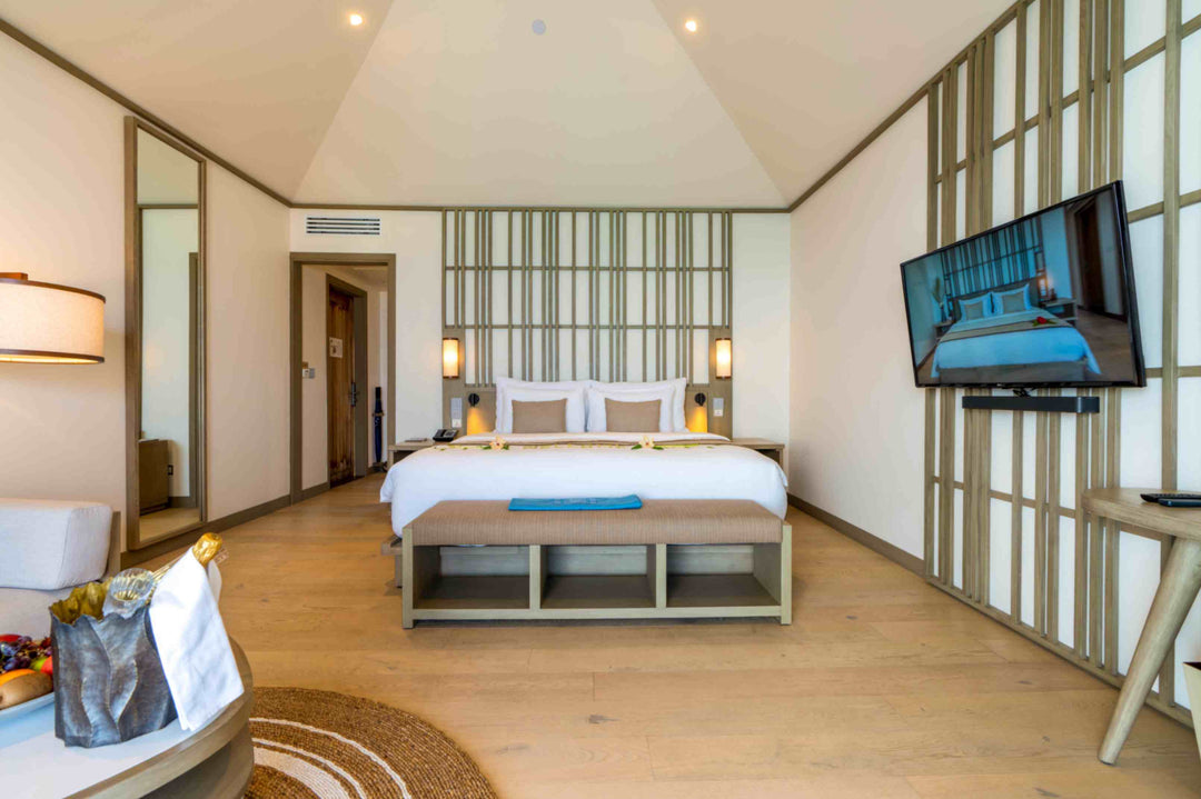 Kagi Maldives Resort &amp; Spa, North Malé Atoll — villa bedroom seen from the seating area, with the king bed, full-length mirror and television on the slatted wall