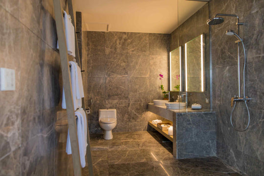 Kagi Maldives Resort &amp; Spa, North Malé Atoll — indoor bathroom lined in dark marble, with a walk-in rain shower, backlit mirrors and a stone vanity