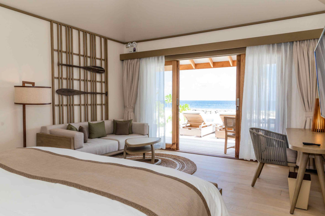 Kagi Maldives Resort &amp; Spa, North Malé Atoll — villa interior looking past the bed and sofa through sliding doors to the deck and the ocean beyond