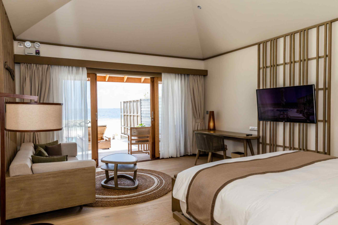 Kagi Maldives Resort &amp; Spa, North Malé Atoll — villa seating area with sofa and round rug, sliding doors open to the terrace and the sea