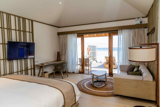 Kagi Maldives Resort &amp; Spa, North Malé Atoll — overwater villa interior looking past the bed and sofa through open doors to the deck and the ocean