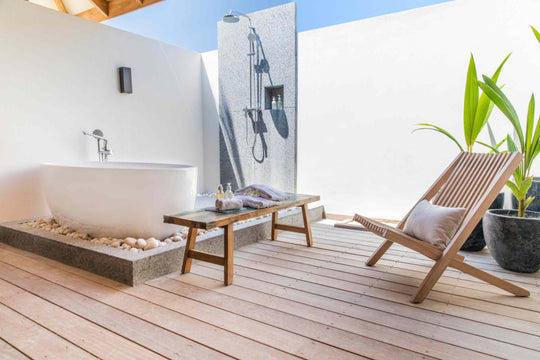 Kagi Maldives Resort &amp; Spa, North Malé Atoll — open-air bathroom with a freestanding tub on pebbles, rain shower and a timber deck chair beside potted palms