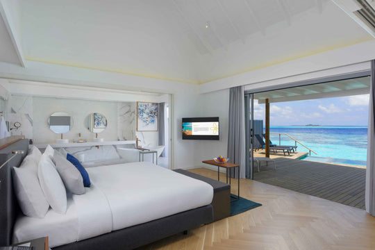 Over-water villa bedroom with king bed, open sliding doors and a deck facing the lagoon