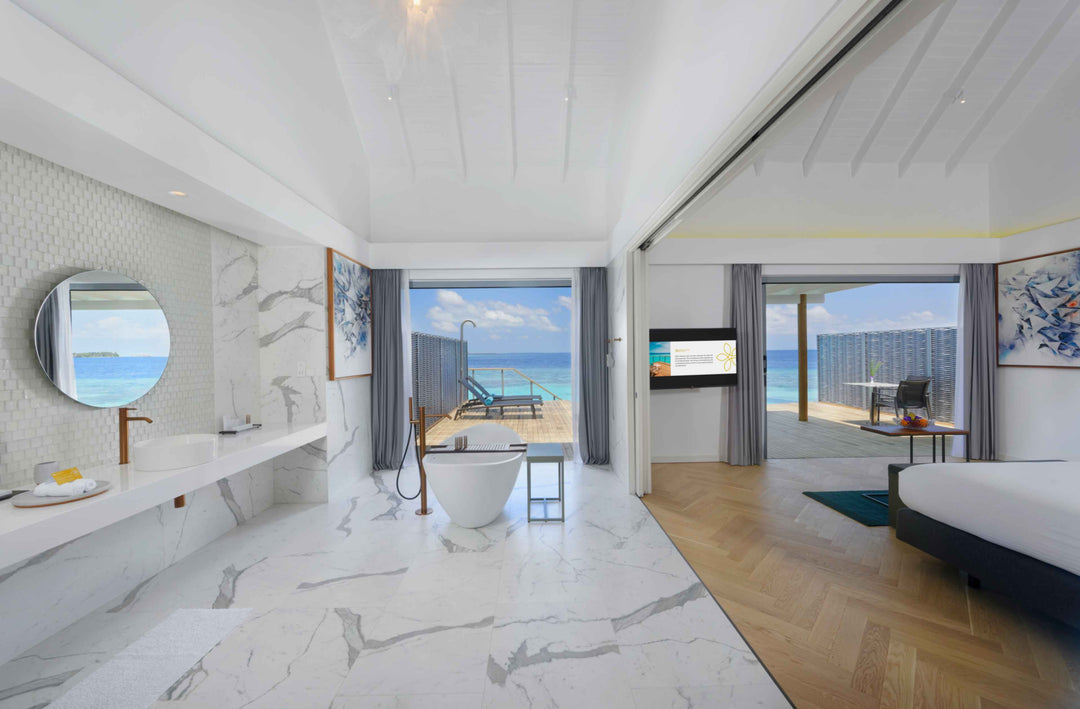 White marble over-water villa bathroom with a freestanding tub open to the bedroom and sea