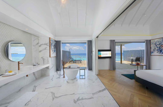 White marble over-water villa bathroom with a freestanding tub open to the bedroom and sea
