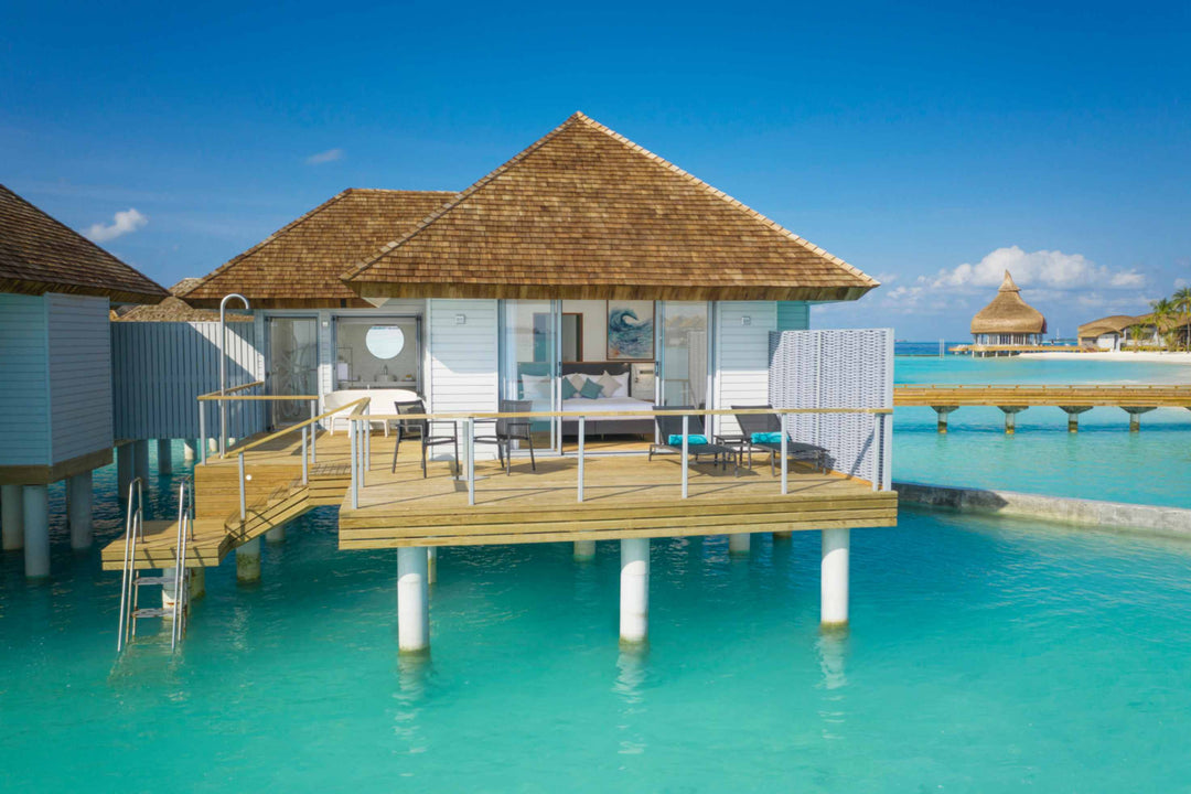 Over-water villa on stilts with a shingled roof, timber deck and ladder into the shallows