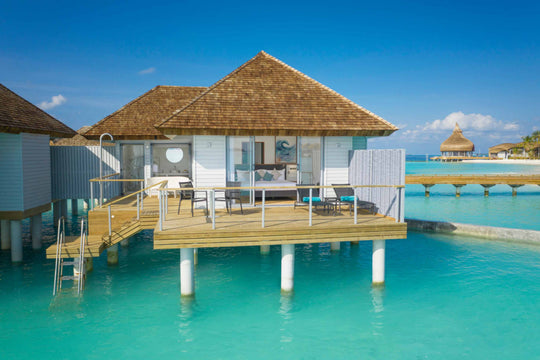 Over-water villa on stilts with a shingled roof, timber deck and ladder into the shallows