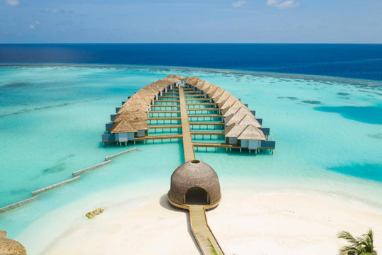 Aerial view of the Maafushivaru over-water villa jetty curving out across the reef