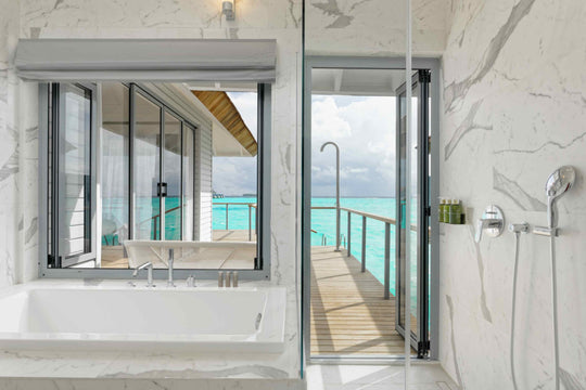 Marble bathroom with a bath below a window, opening onto the villa walkway and the sea