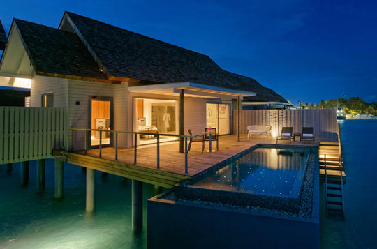 Over-water villa lit at dusk, its private pool glowing beside the timber deck